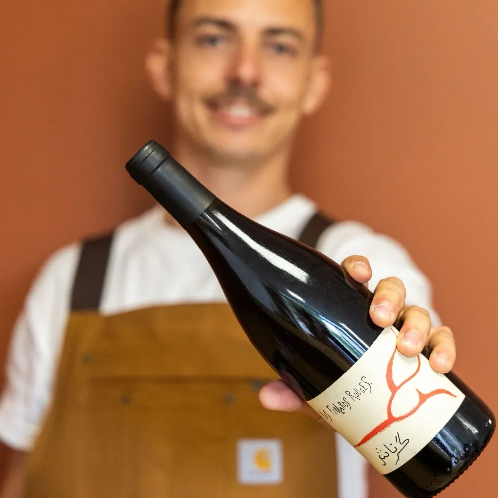 Benjamin Carlier, caviste de La Cave Nectar à Léguevin, tend une bouteille de vin