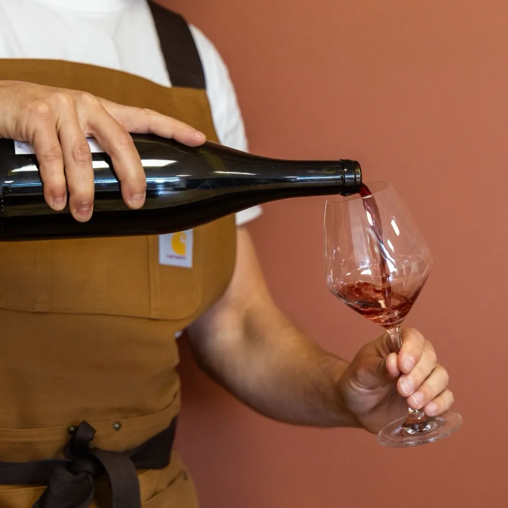 Le caviste de La Cave Nectar sert un verre de vin rouge devant un mur terre de Sienne