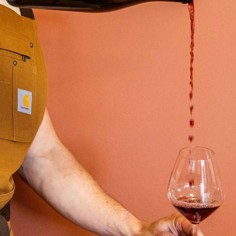 Vin rouge versé dans un verre à La Cave Nectar, fond terre de Sienne